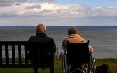 Osoba siedząca na ławce obok osoba siedząca na wózku inwalidzkim